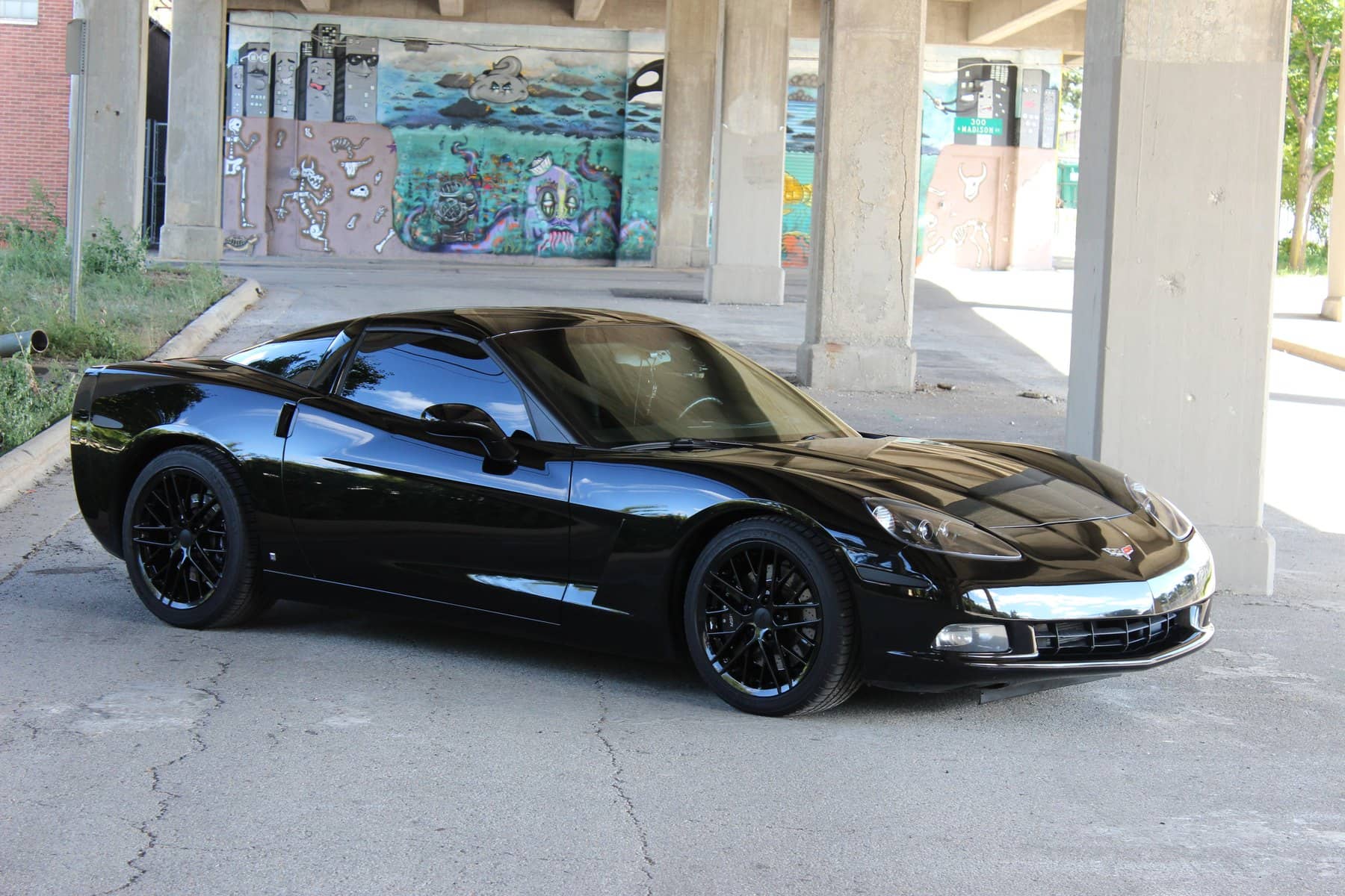 Black Corvette C6, coated, parked under a mural
